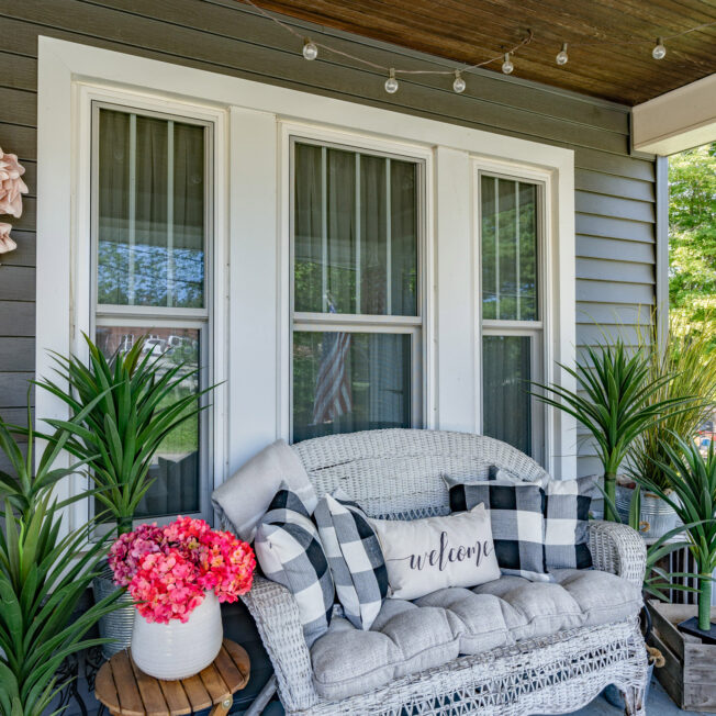 {Porch view of a white Aspect™ double hung window with custom grids and a comfortable outdoor sofa beneath the window; example of double hung windows in ProVia's window gallery}