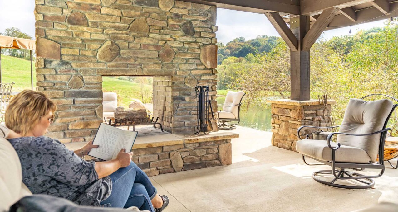 {Woman reading a book outdoors by a manufactured stone veneer fireplace, example of how ProVia stone can be used for different outdoor and indoor applications}