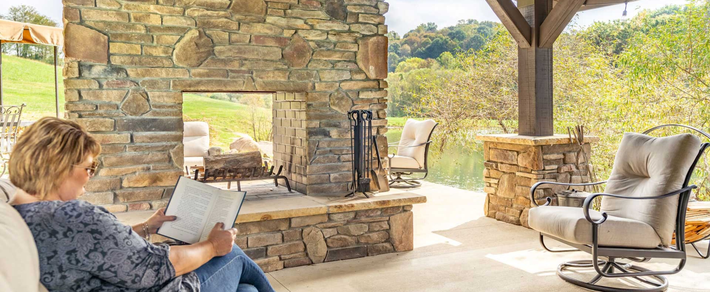{Woman reading a book outdoors by a manufactured stone veneer fireplace, example of how ProVia stone can be used for different outdoor and indoor applications}