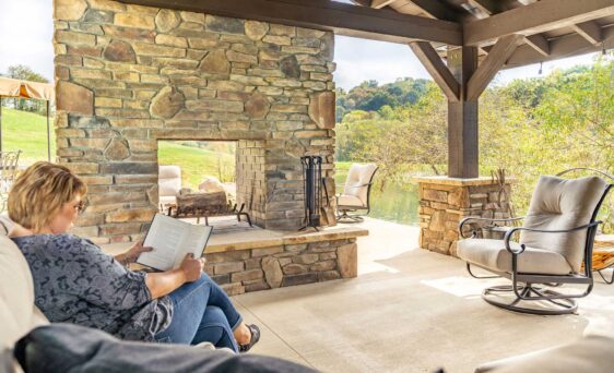 {Woman reading a book outdoors by a manufactured stone veneer fireplace, example of how ProVia stone can be used for different outdoor and indoor applications}