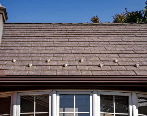 {Closeup photo of a brick home with ProVia's Lodgestone slate metal roofing, a brown color}
