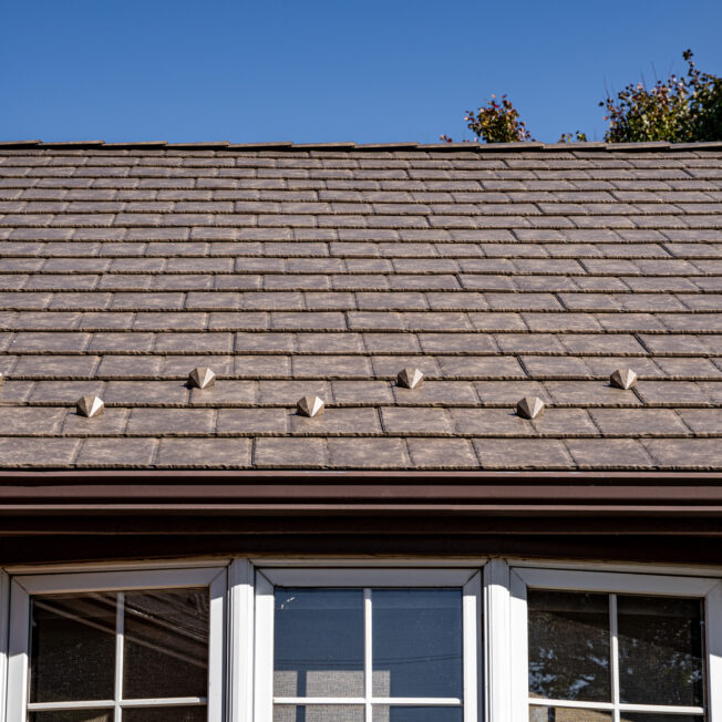 {Closeup photo of a brick home with ProVia's Lodgestone slate metal roofing, a brown color}