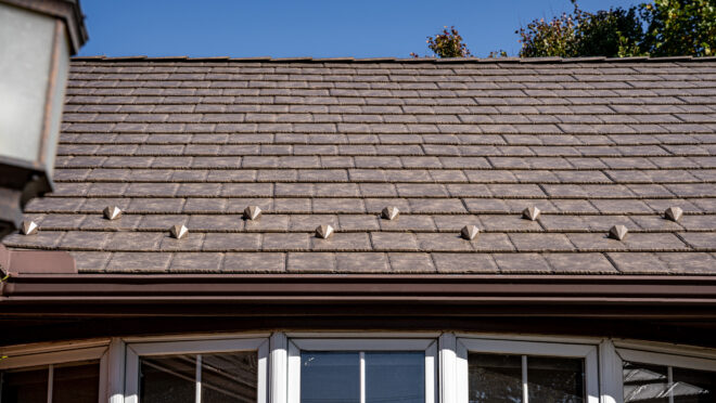 {Closeup photo of a brick home with ProVia's Lodgestone slate metal roofing, a brown color}