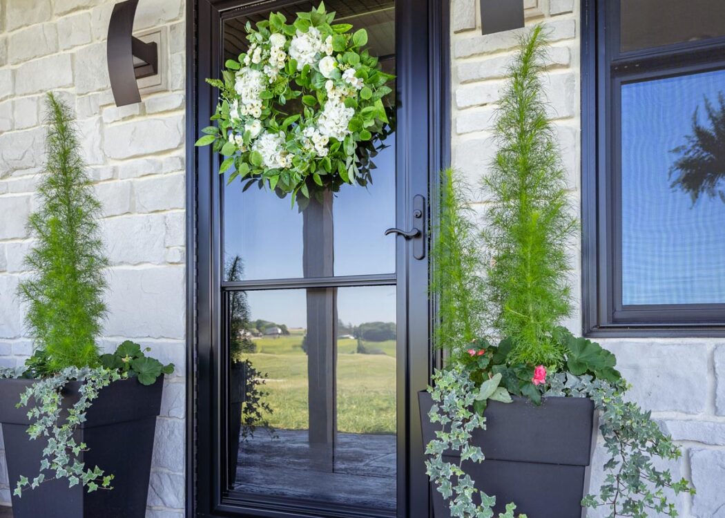 {Spectrum Full View glass storm door in Coal Black over a Signet fiberglass entry door, which contrasts nicely with white stone on a home exterior}