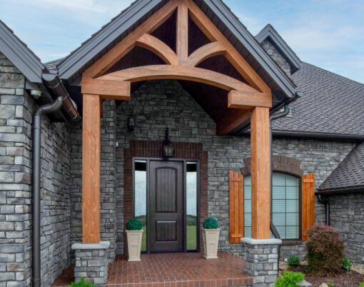 A stone house with timberframe entrance showcasing one of ProVia's Signet 8 foot doors in Knotty Alder in a dark brown Espresso color
