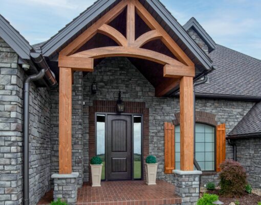 {A stone house with timberframe entrance showcasing one of ProVia's Signet 8 foot doors in Knotty Alder in a dark brown Espresso color}