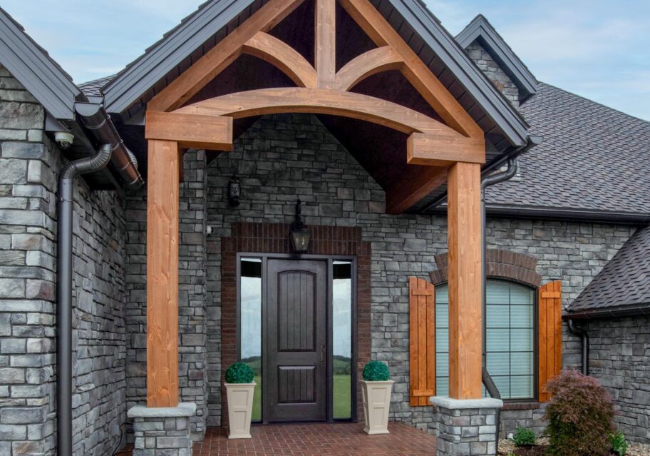 A stone house with timberframe entrance showcasing one of ProVia's Signet 8 foot doors in Knotty Alder in a dark brown Espresso color