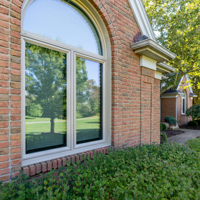 {Exterior view of Aeris™ Casement and Shaped Windows in Sandstone on a brick home}