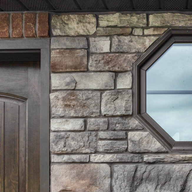 {Stone home exterior with octagon windows with Rustic Bronze finish; example of shaped custom home windows in ProVia's window gallery}