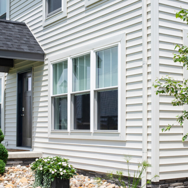{HeartTech vinyl siding in the color White on a two-story home with a portico; main image on ProVia's vinyl siding accessories page}