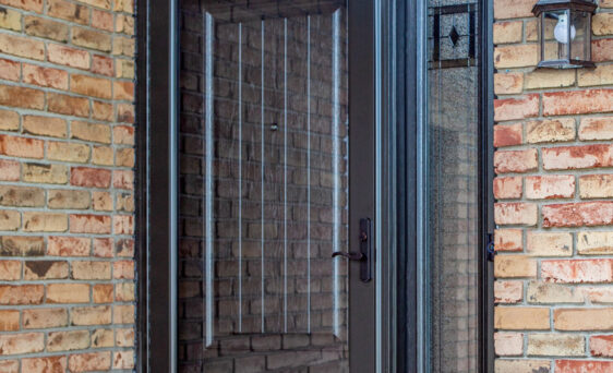 Outside image of a brick home featuring ProVia's Decorator full glass decorative storm door in Rustic Bronze