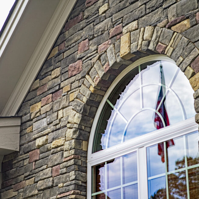 {Closeup of the exterior of a home with an arch shaped window. The exterior features ProVia's Dry Stack stone veneer in the color Huron}