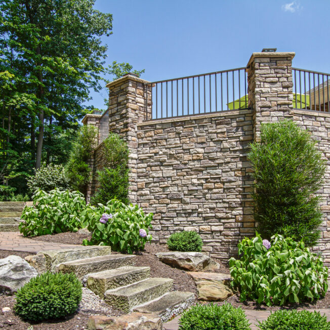 {Photo of an outdoor stone veneer application on a patio area that features ProVia's dry stack stone veneer in the color Seneca, which includes shades of brown stone}