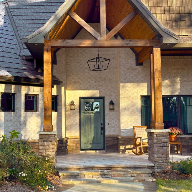 {Brick home with a timber frame entrance, Signet fiberglass door in Rustic Sage, and Shawnee dry stack stone veneer on the bottom of the home and timber frame columns.}