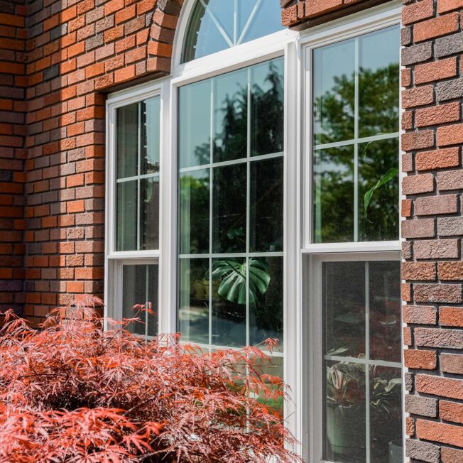 {Exterior view of Endure™ Double Hung, Picture, and Shaped Windows in White with Colonial Grids on a brick home}