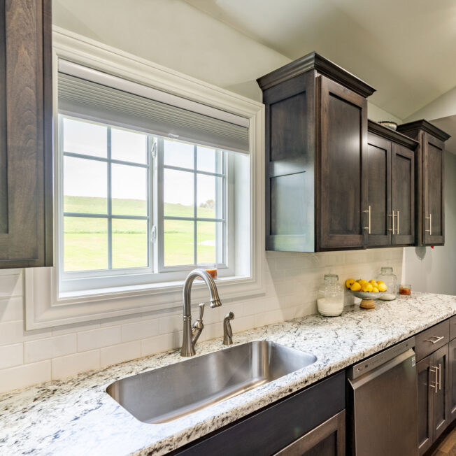 {White sliding windows with cottage-style grids in a kitchen above the sink; example of slider pictures of windows in ProVia's window gallery}