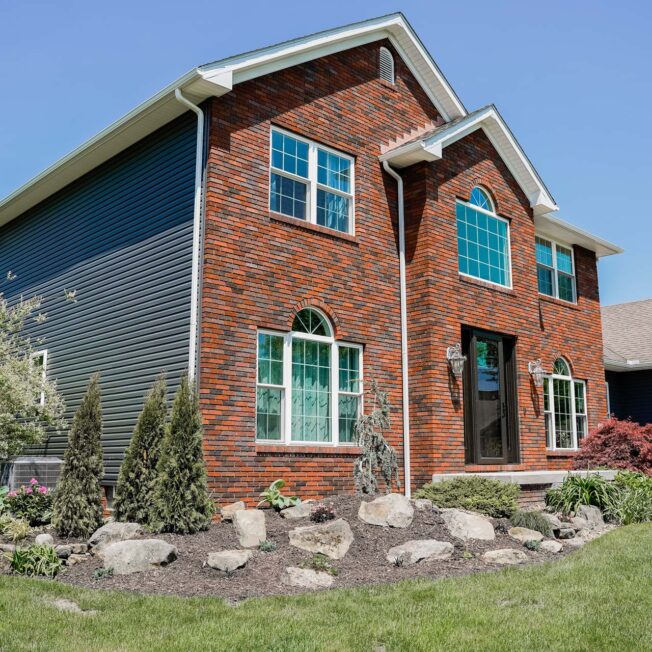 Brick two-story home with HeartTech® Vinyl Siding in Sea Slate and Endure™ Windows in White