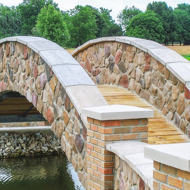 {Arched stone bridge over a stream featuring Shenandoah field stone veneer}