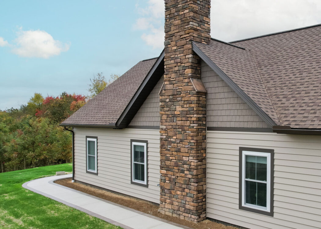 {Aerial view of ProVia Harbor Mill™ Shake in Pueblo and CedarMAX® D6 Vinyl Siding in Clay on the side of a home with a chimney}