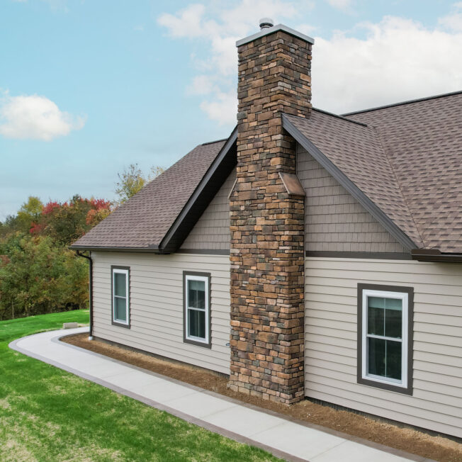 {Aerial view of ProVia Harbor Mill™ Shake in Pueblo and CedarMAX® D6 Vinyl Siding in Clay on the side of a home with a chimney}
