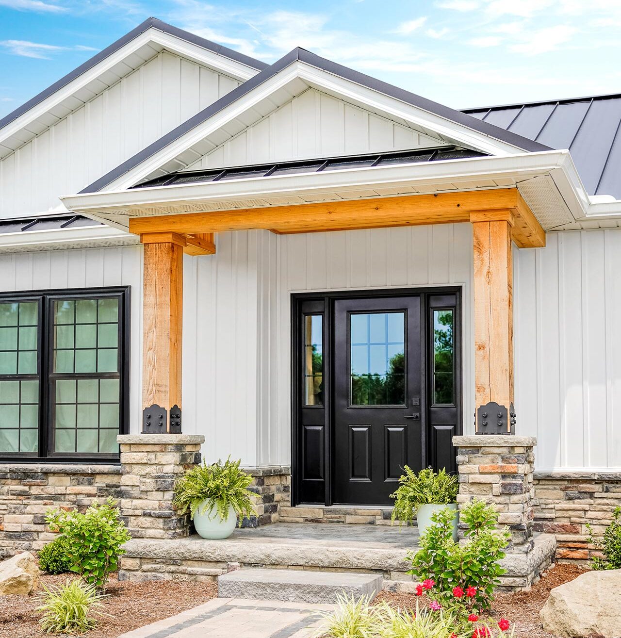 A white house with a porch with stone columns and timber and a Legacy™ Smooth 430 entry door in Coal Black with sidelites