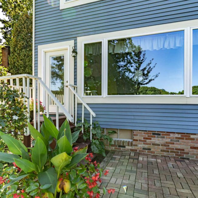 {Exterior view of a blue house with large windows, combination of  picture windows and casement windows on each side}