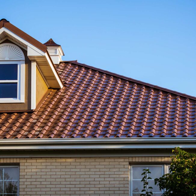{Exterior view of ProVia Barrel Tile Metal Roofing in Terracotta on a light brick home with a stucco dormer}