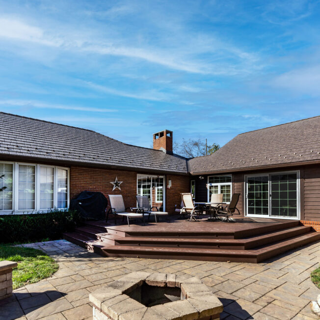 {Photo of the back side of a brick home with a deck. Home features ProVia's Lodgestone slate metal roofing, a brown color}