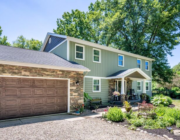 {Two-story home with green ProVia vinyl siding blended with manufactured stone veneer in a blend of browns and tans}