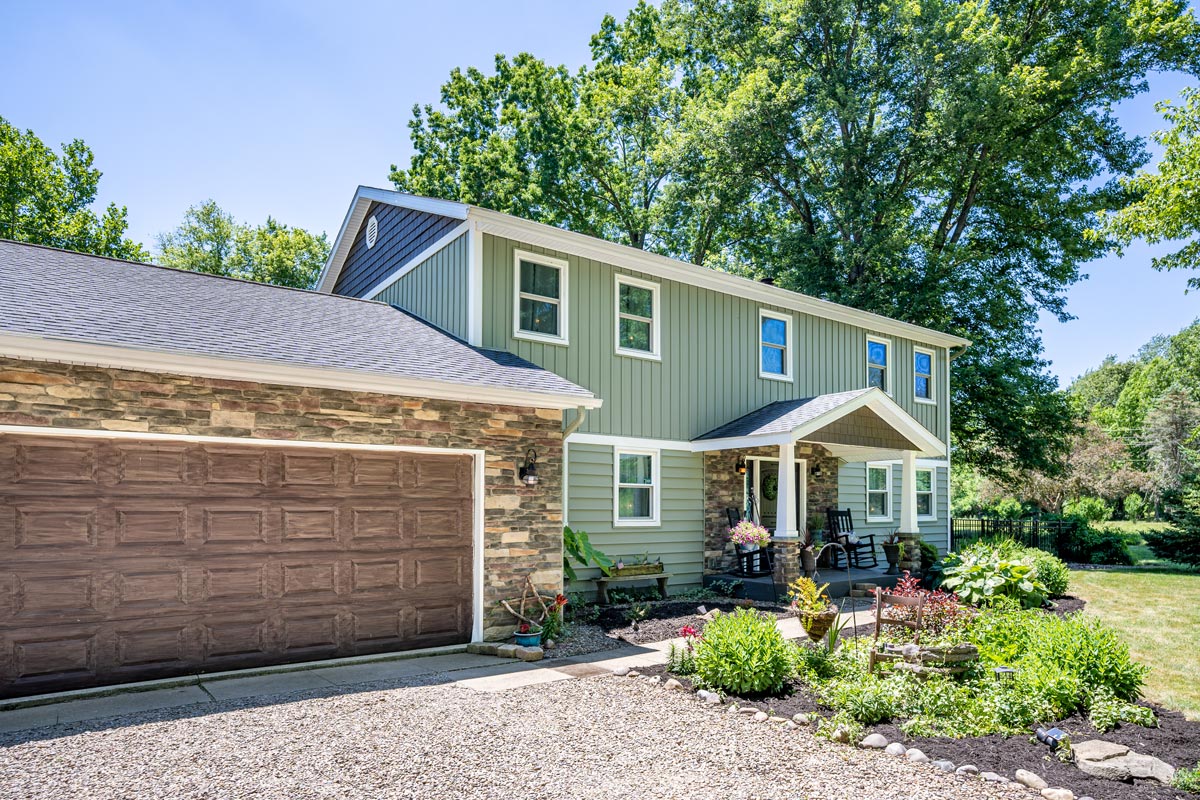 Two-story home with green ProVia vinyl siding blended with manufactured stone veneer in a blend of browns and tans