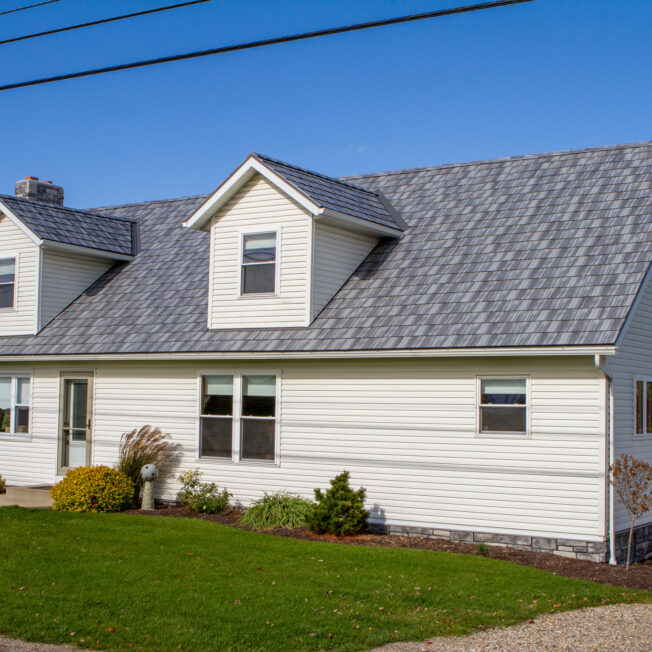 {Photo of a cape cod style home with gray Pepperwood Shake metal roofing—a metal shingle roof that resembles the look of shake}