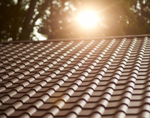 {Closeup view of a home with ProVia's new metal barrel tile roof in Terracotta with the setting sun behind it, example of metal roofing that looks like clay tile}