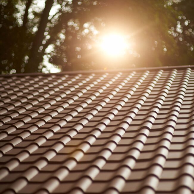{Closeup view of a home with ProVia's new metal barrel tile roof in Terracotta with the setting sun behind it, example of metal roofing that looks like clay tile}