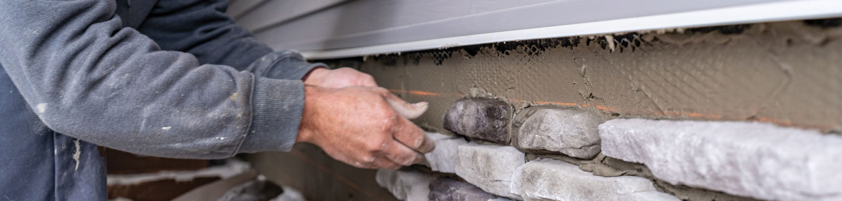 Closeup of a stone mason installing ProVia manufactured stone on a home