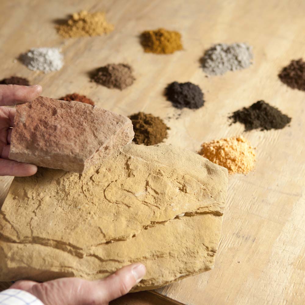 Man holding two stones with Manufactured Stone Color Pigments in the background on a wooden surface
