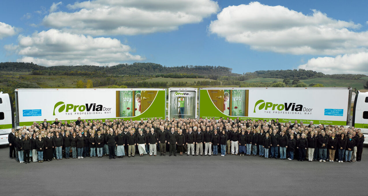 {A group photo of ProVia employees in 2007 standing in front of two ProVia semi trucks}