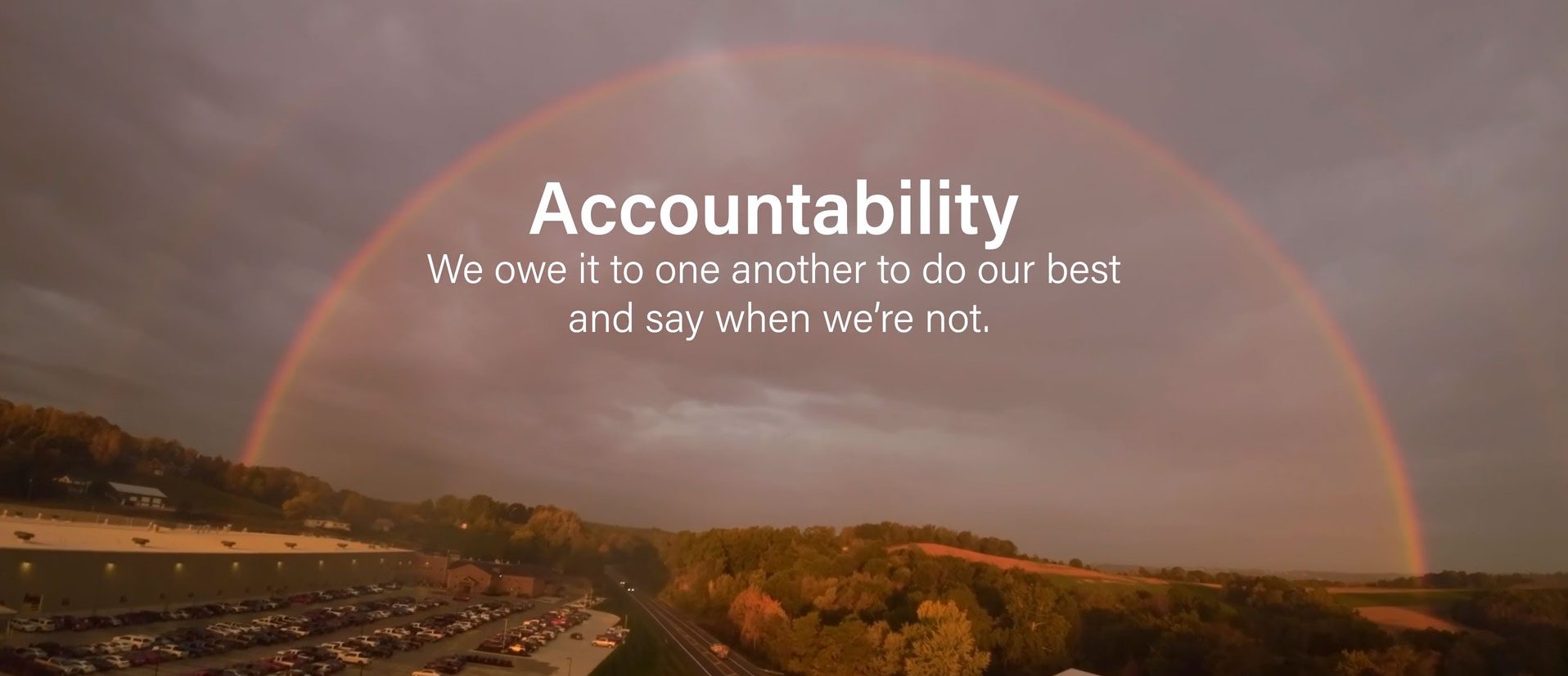 Image of a rainbow over some trees, a highway, and a parking lot with the words: "Accountability—We owe it to one another to do our best and say when we're not."