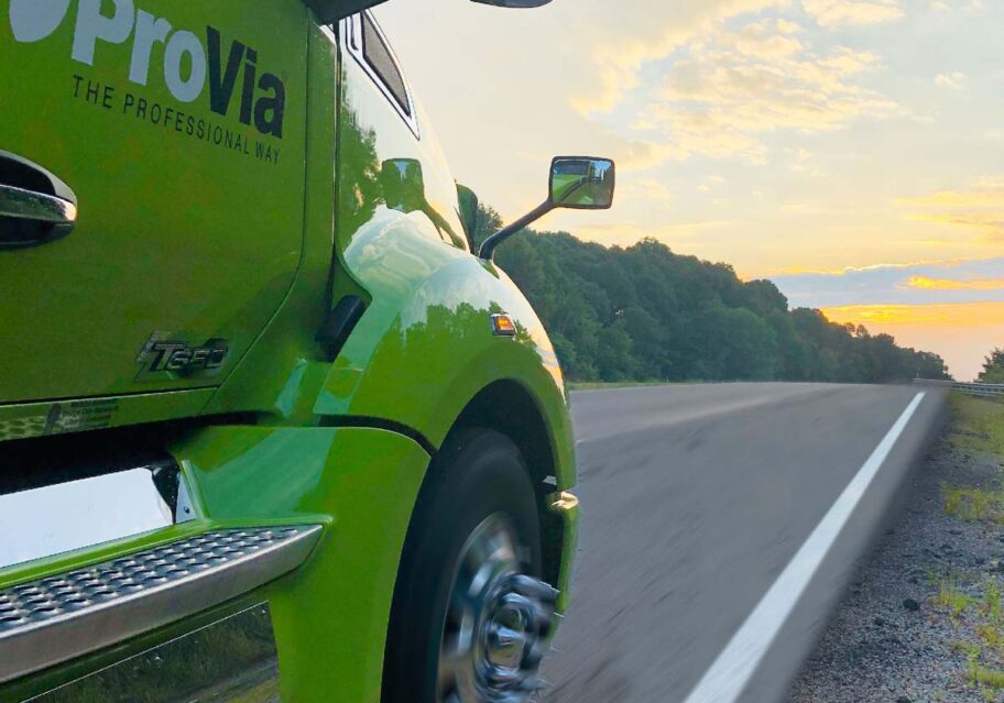 Side view of a Provia semi truck cab as the truck drives down a road at sunrise