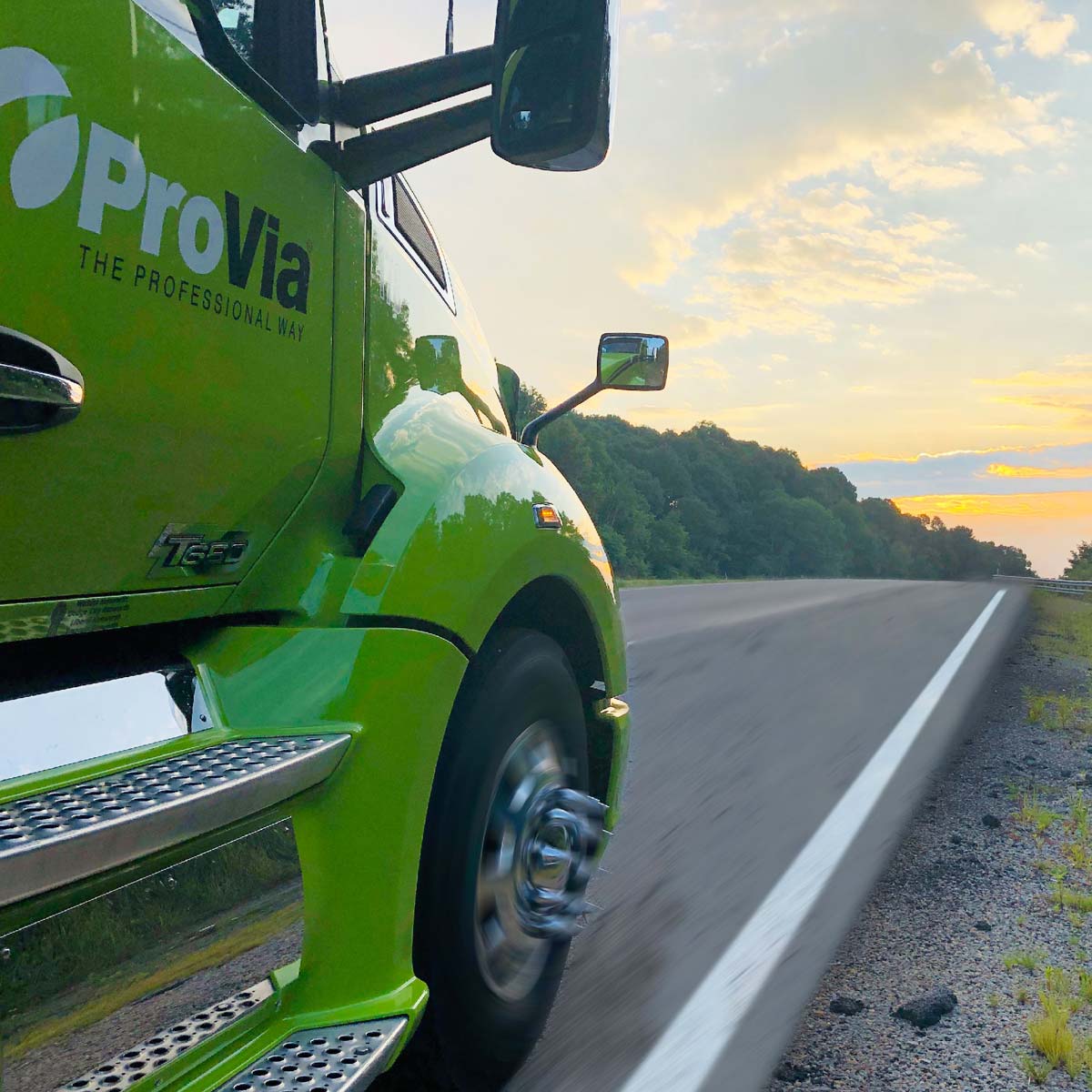 Side view of a Provia semi truck cab as the truck drives down a road at sunrise