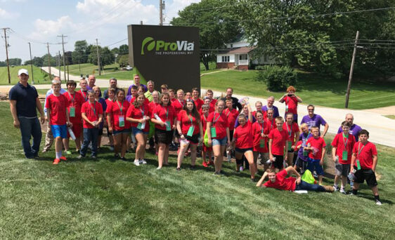 {Group of students in red shirts outside ProVia in front of the ProVia sign. These students participated in the 2017 Manufacturing Camp at ProVia.}