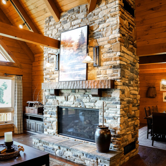 {Cozy interior image of a log cabin living room with ProVia Fieldstone Strathmore manufactured stone with Ledgestone Brighton manufactured stone fireplace}