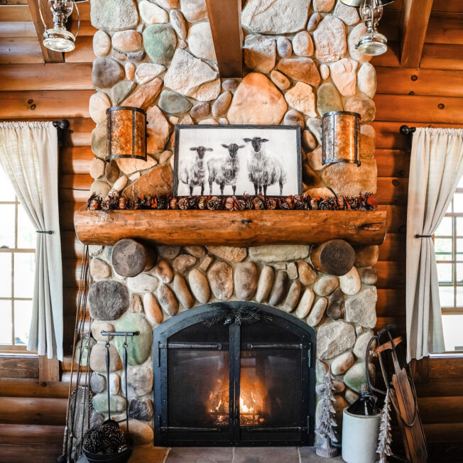 {Cozy interior image of a log cabin fireplace with ProVia Mountain River Rock manufactured stone on a fireplace}
