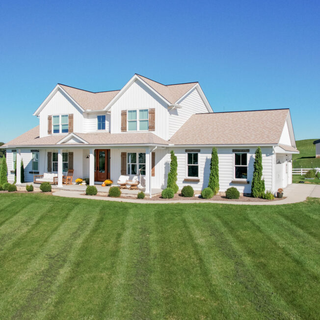 {CedarMAX® Board and Batten and double 6″ insulated vinyl siding in White on a two-story home in the country}