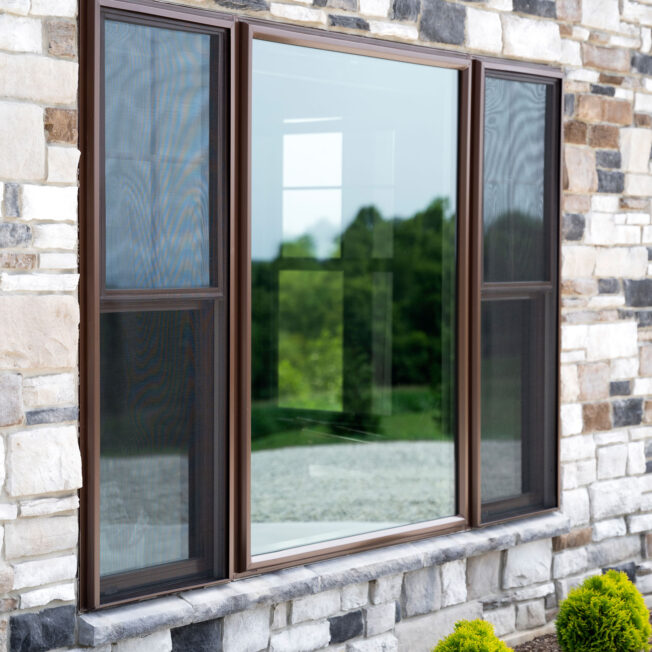 {ProVia® Endure™ double hung windows and picture windows in Tudor Brown with Cottage Grids on a home exterior with ProVia Terra™ Cut manufactured stone in the color Niagara}