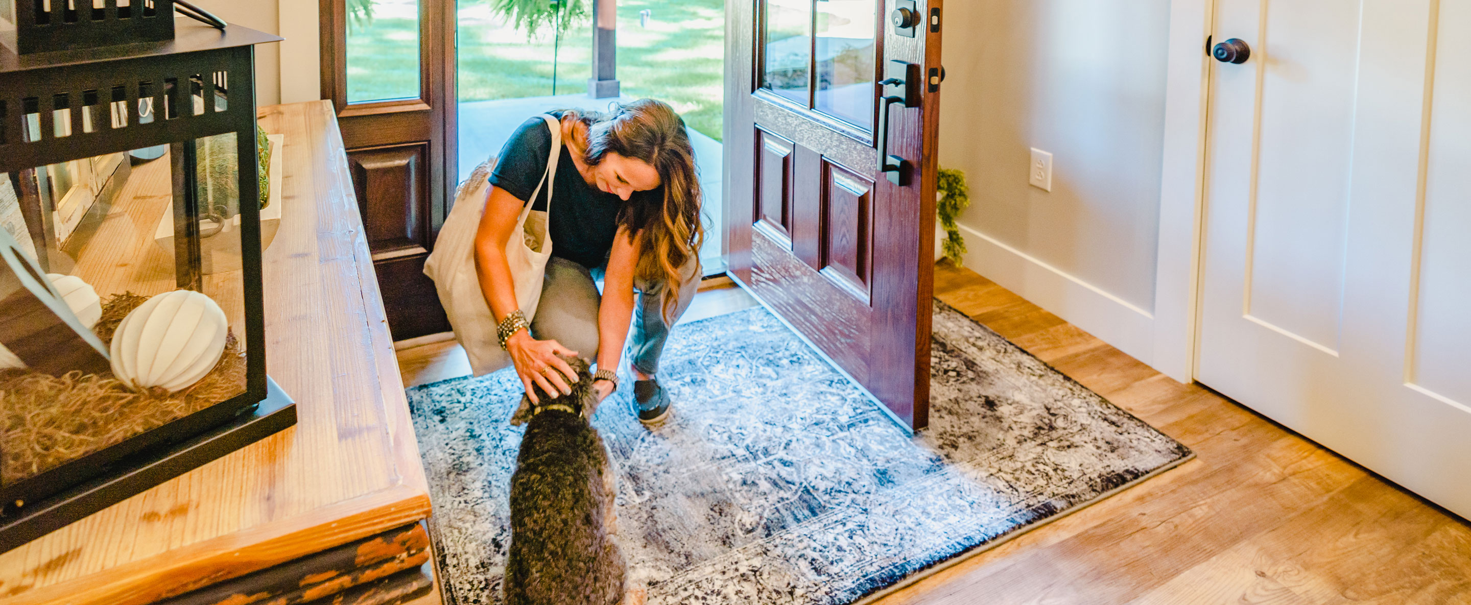 Photo of a woman kneeling down to pet a dog in her entryway, which shows an example of exterior doors with a fiberglass entry door and sidelights, example of ProVia® exterior replacement doors and door exterior options.