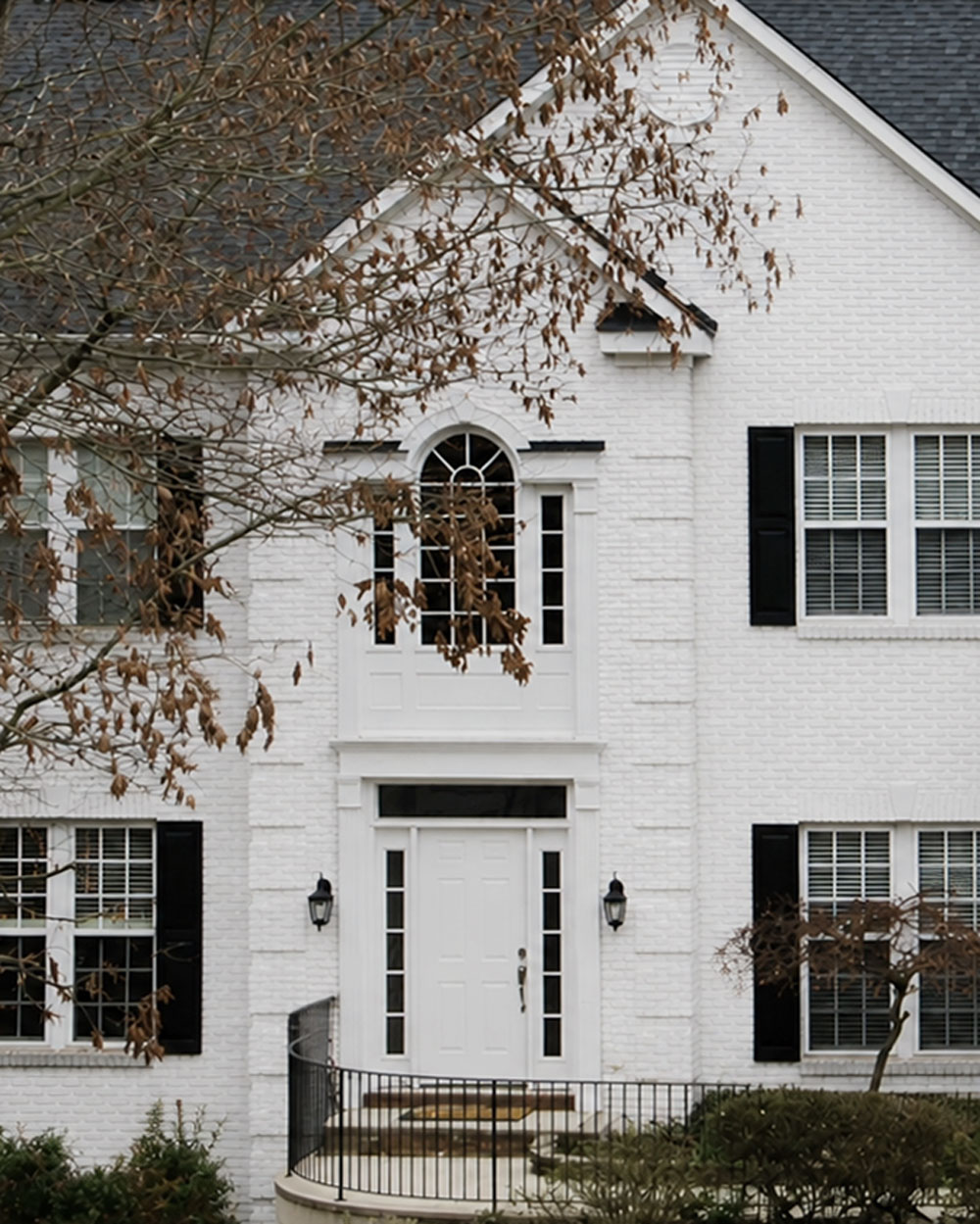 Exterior view of the front of a white colonial style home with a white entry door before getting a new door