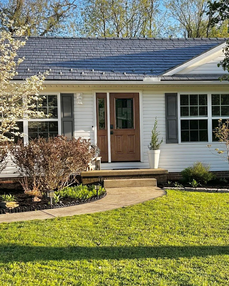 Outside view of a white ranch home with ProVia® Baystone Slate Metal Roofing and a Signet® Oak 430 Entry Door and 130 Sidelite in Caramel stain