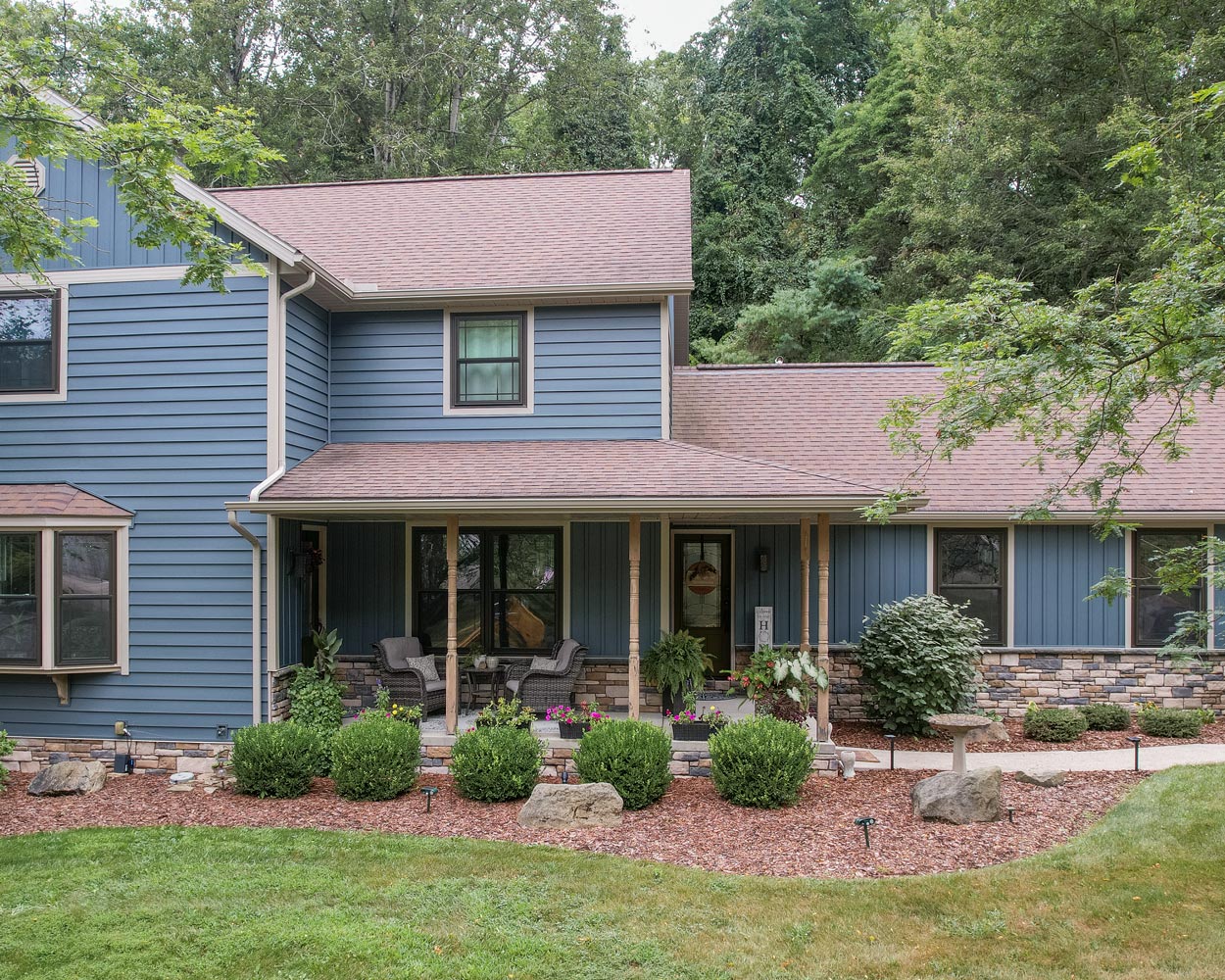 Exterior view of the front of a home after getting new ProVia® CedarMAX® Insulated Vinyl Siding and Board and Batten in the color Sea Slate,  Endure™ Double Hung Windows in Classic Bronze, and Summit Terra Cut™ manufactured stone